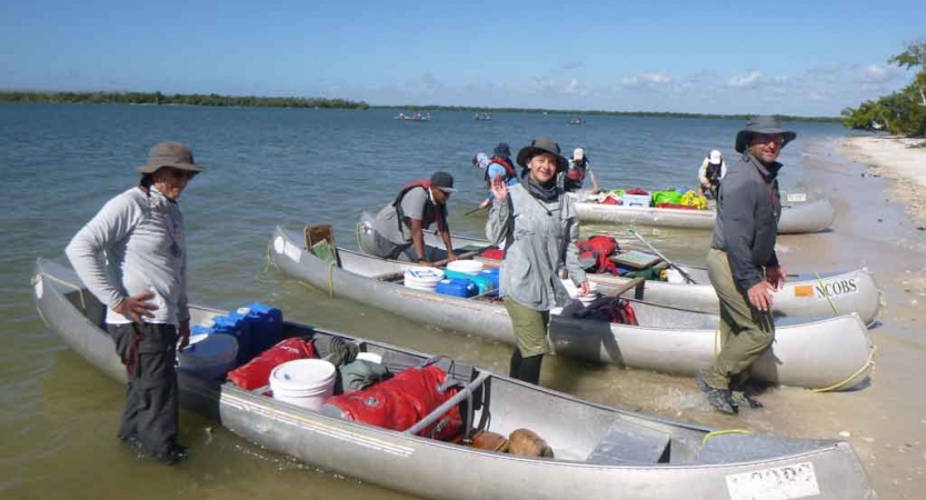 participants stand beside canoes resting on a beach on a family expedition with outward bound